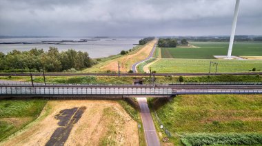 27 Mayıs 2025 - Moerdijk-Hollanda: Hollands Diep yakınlarındaki Dike Geçidi 'ndeki Moerdijk demiryolu köprülerinin hava görüntüsü. Yeşil nehir kıyıları, yol, viyadük ve su görünür..