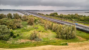 27 Mayıs 2025 - Moerdijk-Hollanda: Kara bulutlar altında Hollands Diep 'i geçen Moerdijk demiryolu ve karayolu köprülerinin havadan görünüşü. Yeşil nehir kıyıları ve görünür su.
