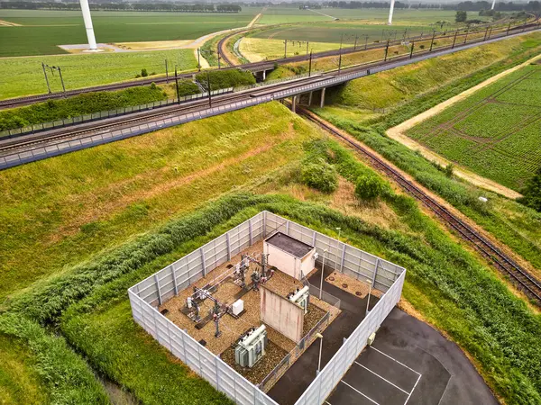 27 Mayıs 2025 - Moerdijk-Hollanda: Moerdijk demiryolu köprüsü yakınlarındaki bir tren istasyonunun havadan görüntüsü, yeşil alanlar ve bulutlu bir gökyüzü altında modern rüzgar türbinleriyle çevrili.