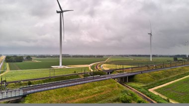 27 Mayıs 2025 - Moerdijk-Hollanda: Moerdijk 'in açık kırsalındaki rüzgar türbinlerinin yakınındaki yüksek hızlı demiryolunun altından geçen bir demiryolu lokomotifi.