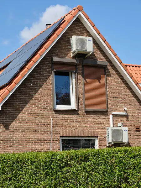 22 Mayıs 2025 - Oosterland-Hollanda: Oosterland köyünün ön cephesinde modern güneş panelleri ve klima üniteleri olan geleneksel Hollanda tuğla evi.