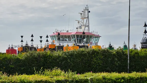 28 Mayıs 2025 - Vlissingen-Hollanda: Hollanda Sahil Güvenlik gemisi Vlissingen limanındaki bir şamandıraya demirlemiş renkli seyrüsefer şamandıraları çitin arkasındaki rıhtımda depolanmış.