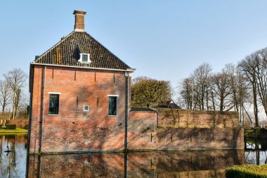 9 Mart 2025 - Leens-Hollanda: Leens 'te tarihi bir tuğla köşk olan Borg Verhildersum, açık mavi gökyüzü altında yapraksız budanmış ağaçlar, köprüler ve hendekler..
