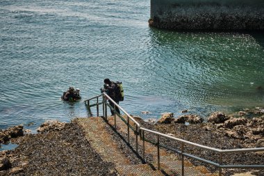 20 Mayıs 2025 - Zierikzee-Hollanda: İki scuba dalgıcı popüler Zeelandbrug dalış sahasında sudan merdivenlere tırmanıyor, sualtı dalış oturumlarını bitiriyorlar.
