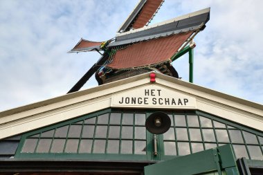 13 Nisan 2025 - Zaandam-Hollanda: Zaanse Schans 'taki tarihi kereste fabrikası Het Jonge Schaap geleneksel kış yelkenleri ile parçalı bulutlu bir bahar günü.
