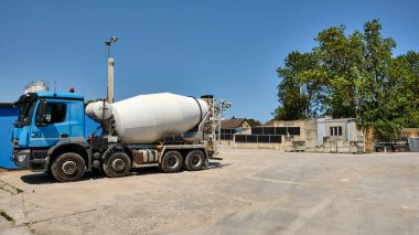 14 Haziran 2025 - Benz-Almanya: Beton santral alanında beton depolama duvarlarına dikey güneş panelleri monte edilmiş mavi çimento kamyonu endüstride sürdürülebilir enerji kullanımını gösteriyor.