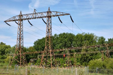 Ağaçlar ve aşırı gelişmiş bitki örtüsüyle çevrili Peenemuende yakınlarındaki kullanılmayan elektrik santralinde paslanmış yüksek voltajlı sütunlar ve izolatörler..