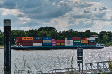 2 Haziran 2025 - Tolkamer-Hollanda iç konteynır gemisi bulutlu bir gökyüzü altında renkli yük konteynerleriyle dolu Ren nehri üzerindeki Rotterdam 'dan Almanya' ya doğru yola çıktı..