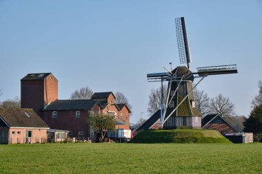 28 Mart 2025 - Miste-Hollanda: Achterhoek bölgesindeki tarihi Meenkmolen yel değirmeni, kırsal köy evleriyle çevrili, tahıl öğütmek için kullanılan tipik bir Hollanda kemer değirmeni.