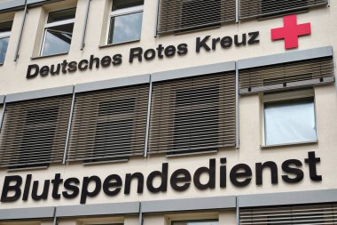 23 Haziran 2024 - Neubrandenburg-Almanya: DRK Kan Bağış Hizmetleri binasının dış cephesinde logo ve Alman Rotes Kreuz imzalı pencere gölgeli bej bir cephede.
