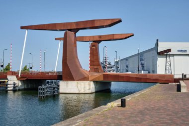 30 Mayıs 2025 - Vlissingen-Hollanda: Arka planda Damen tersanesi ve lüks yatıyla Vlissingen limanındaki modern korten çelik asma köprü.