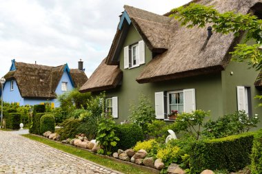 9 Temmuz 2025 - Putgarten-Almanya: Renkli cepheli geleneksel sazdan çatı evleri ve sakin bir sahil köyünde kaldırım taşı caddesi boyunca yemyeşil bahçeler.