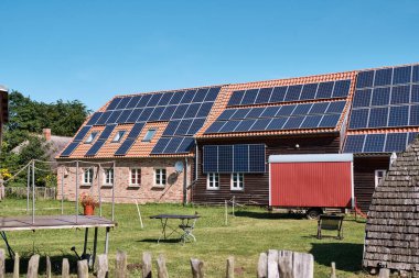 16 Temmuz 2025 Klockenhagen - Almanya: Güneş panelleri açık hava müzesindeki tarihi bir çiftlik evinin çatısını ve maskesini kaplayarak, maksimum yenilenebilir enerji kullanımını gösteriyor.