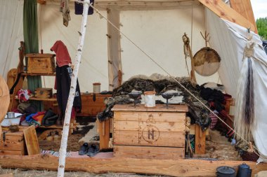 9 Temmuz 2025 - Putgarten-Almanya: Yatağında hayvan postları olan bir Viking canlandırma çadırının içi, rün oymaları olan ahşap bir sandık ve davul ve alet gibi geleneksel eşyalar.