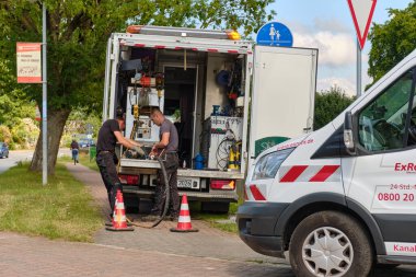 14 Temmuz 2025 - Klockenhagen-Almanya: İki teknisyen, açık hava boru bakım operasyonları sırasında şirket minibüslerinin yanında bir kanalizasyon temizleme robotunu inceliyor.