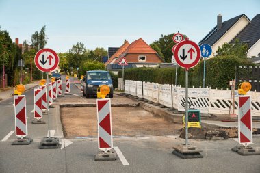 16 Temmuz 2025 Sievershagen - Almanya: İşçi karavanıyla yol çalışması sahnesi, güneş paneli çatıları olan bir yerleşim bölgesinde güvenlik bariyerleri ve tabelalar.