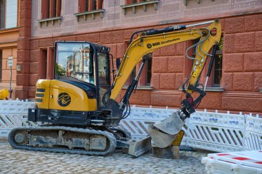 18 Temmuz 2025 Rostock Üniversitesi - Almanya: Bir yol inşaatında hafta sonu için park edilmiş kompakt kazıcı, hırsızlığı önlemek ve güvenlik bariyerleriyle çevrili çoklu kovalarla.