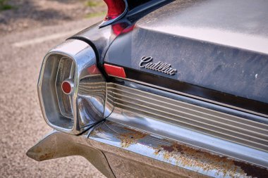 17 Ağustos 2024 - Görünür pas ve yaşlanma belirtileriyle krom kuyruk yüzgeci, stop lambası ve amblemi gösteren klasik bir Cadillac 'ın arka ucu yakın plan görüntüsü.