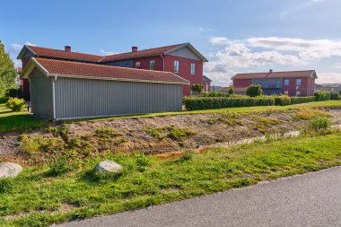 Viken, İsveç; 10 Ağustos 2025: Güneşli bir yaz gününde çağdaş bir yerleşim bölgesinde gri kulübesi ve hendeği olan modern kırmızı ahşap apartmanlar.