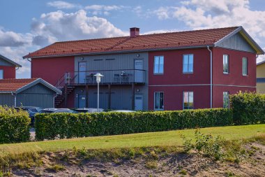 Viken, İsveç; 10 Ağustos 2025: Güneşli bir yaz gününde çağdaş bir yerleşim bölgesinde balkonu ve çiti olan modern kırmızı ahşap apartman.