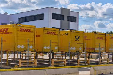 Winsen, Germany ; September 30, 2025: Row of DHL logistics containers parked at Amazon distribution center site, symbolizing global parcel delivery, e-commerce transport and supply chain.