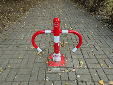 Canlı kırmızı ve beyaz bir durak bariyeri kaldırımlı bir yola yerleştirilmiş, düşen yapraklarla çevrili, yayalara yaya geçidinde dolaşırken durmaları ve güvenliklerini sağlamaları için işaret ediliyor..