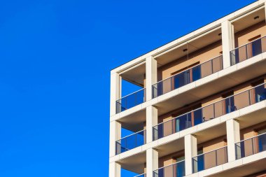 Çağdaş, balkonlu bir bina parlak mavi bir gökyüzüne karşı duruyor. Parlak tasarımını ve yapısını sergiliyor..