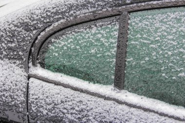 Snow covers the surface of a parked car, highlighting the cold winter atmosphere and icy conditions outside.