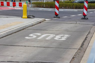 Beyaz Otobüs Metin İşaretli Beton Otobüs Yolu Bölümü ve Yoldaki Kırmızı Beyaz Güvenlik Engelleri