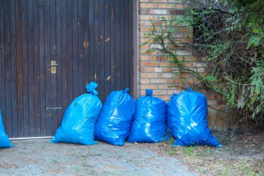 Şehir merkezinde tuğla duvarın yanında Koyu Ahşap Kapıya Sıralanmış Mavi Çöp Torbaları