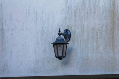 Açık gri duvar üzerine monte edilmiş klasik siyah dış duvar feneri minimalist mimari ayrıntılar yaratıyor.