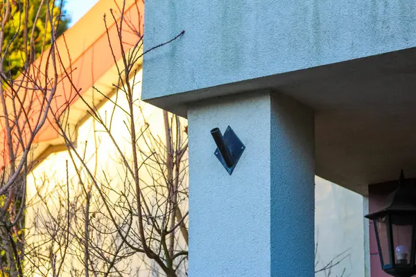 Açık mavi bina cephesine yerleştirilmiş dekoratif siyah duvar feneri. Sıcak turuncu güneş ışığı kontrastı oluşturuyor.