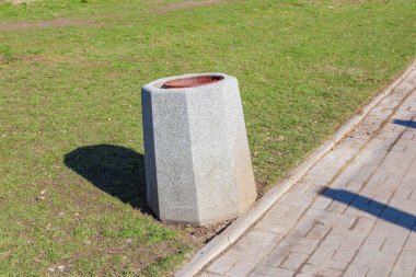 Çimenli alanda kırmızı başlıklı beton Bollard, Kamu Parkındaki tahta kaldırımın yanında.
