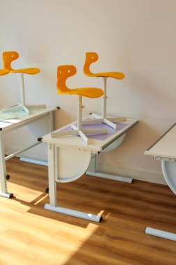 Boş Sınıfta Ahşap Zemin ve Doğal Işıklı Modern Portakal ve Beyaz Öğrenci Masaları