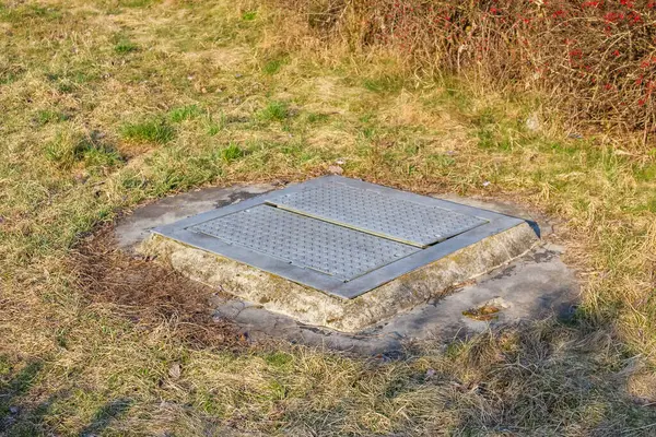Hava delikleriyle Beton Kanalizasyon Kapağı Su Yönetimi İçin Bahar Sebzeleri Arasında Çimenli Arazi