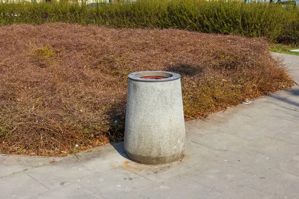 Paved Yolu 'ndaki beton atık çöp kutusu Şehir Parkı Ayarlarında kurumuş peyzaj ile