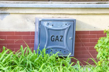 Kırmızı Tuğla Duvarda GAZ etiketli Gri Gaz Yardım Kutusu Yeşil Tesislerle çevrili