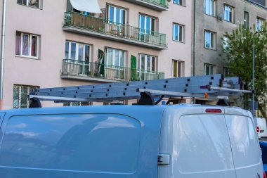 Çatı Rack 'i olan Mavi Ticari Minibüs Konut Apartmanına yakın bir yere park edilmiş.