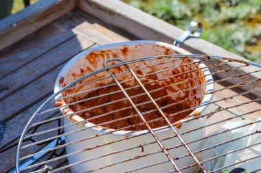 Ahşap masada pişmiş etle birlikte yuvarlak metal ızgara. Açık hava barbekü hazırlıklarını gösteriyor.