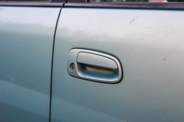Açık mavi aracın gümüş kapı kolunun yakın görüntüsü minimal tasarım ve pürüzsüz yüzey gösteriyor