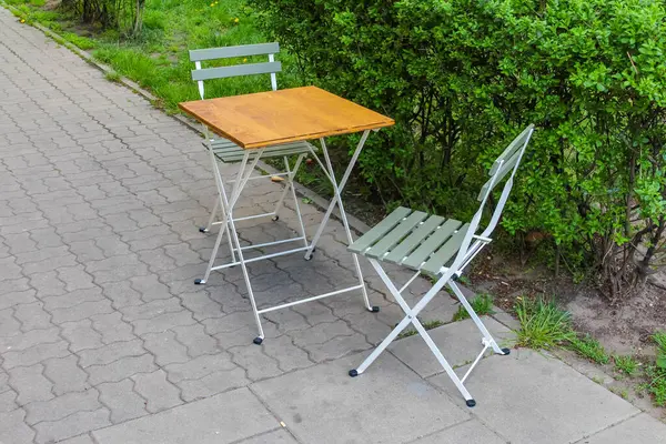 Açık Cafe Masa ve Sandalyeler, Bahçe Bahçesinde Tahta Yüzey, Yeşil Çalılarla çevrili.