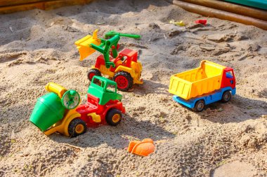 Yaratıcı çocuk oyunları için kum havuzuna yerleştirilmiş renkli plastik inşaat oyuncakları ve çöp kamyonları koleksiyonu