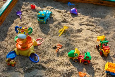 Çeşitli renkli plastik hayvan ve inşaat oyuncakları kumlu oyun sahasına saçılmış canlı çocuklar için oyun sahneleri yaratıyor.