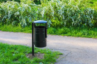 Kentsel eğlence alanında atık yönetimi sağlayan yeşil park yolu boyunca yerleştirilen siyah umumi çöp kutusu