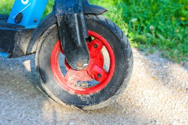 Çakıl yolundaki elektrikli scooter 'ın kırmızı tekerleğinin dış mekandaki ulaşım detaylarını gösteren yakın çekimi