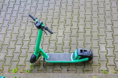 Turkuaz elektrikli scooter gündüz vakti kaldırımda parkedildi.