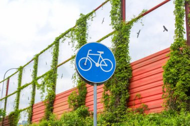 Kentsel çevrede yeşil çitlere asılmış mavi dairesel bisiklet yolu tabelasının yakın çekimi