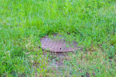 Lush Green Grass Alanındaki Yuvarlak Metal Kanalizasyon Kapağı Endüstriyel ve Doğal elementler arasında Karşıtlık Oluşturuyor