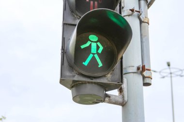 Yeşil yürüyen figürle trafik ışığından geçen yayalar açık gri şehir arka planına karşı