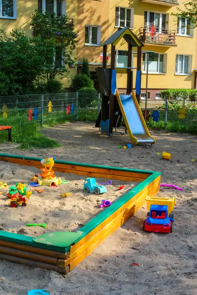 Kum havuzlu renkli çocuk parkı, tırmanma ekipmanları ve konut binalarıyla çevrili kaydırak.